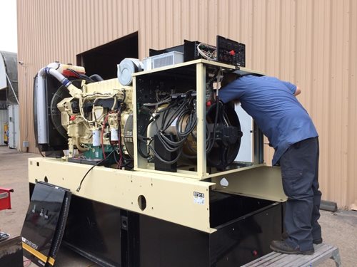 A man repairs a generator outside a building, focused on his task amidst tools and equipment.